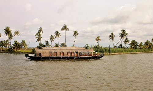 Scenic Kerala houseboat gliding through serene backwaters with palm trees and vibrant sunset sky.