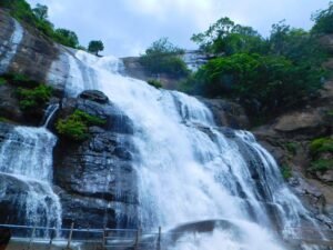 Kutralam Main Falls surrounded by lush green hills during monsoon season, Tamil Nadu